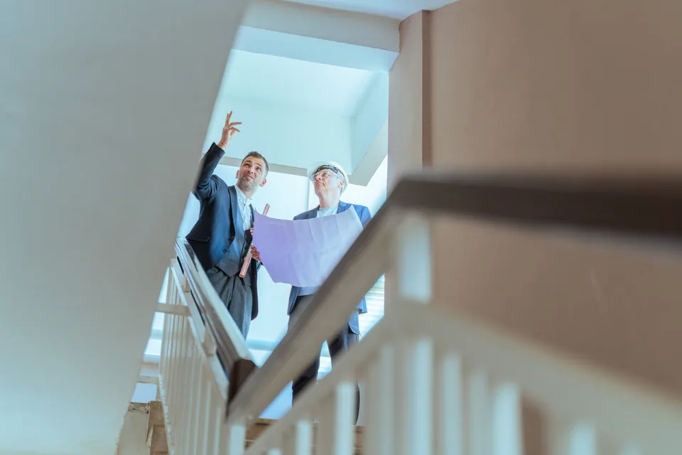 Zwei Personen besichtigen ein Treppenhaus und besprechen einen Plan
